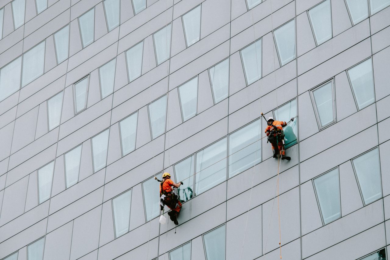 High-rise window washers in safety gear cleaning a skyscraper facade.